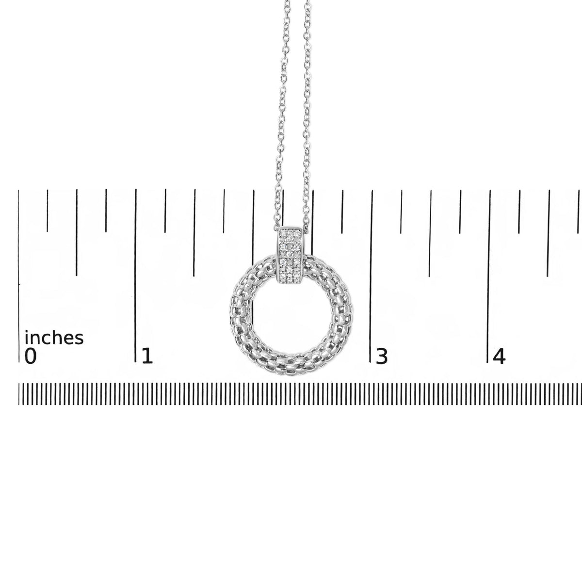 Close-up front view of a white metal circular necklace pendant with a micro-pave setting of white round gemstones on the top part, shown on a measurement scale.