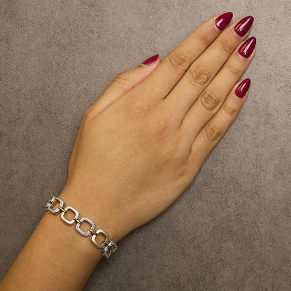 Bracelet with alternating yellow and white metal square links, some set with small white gemstones in pave setting, shown worn on a model's wrist, top-down angle.