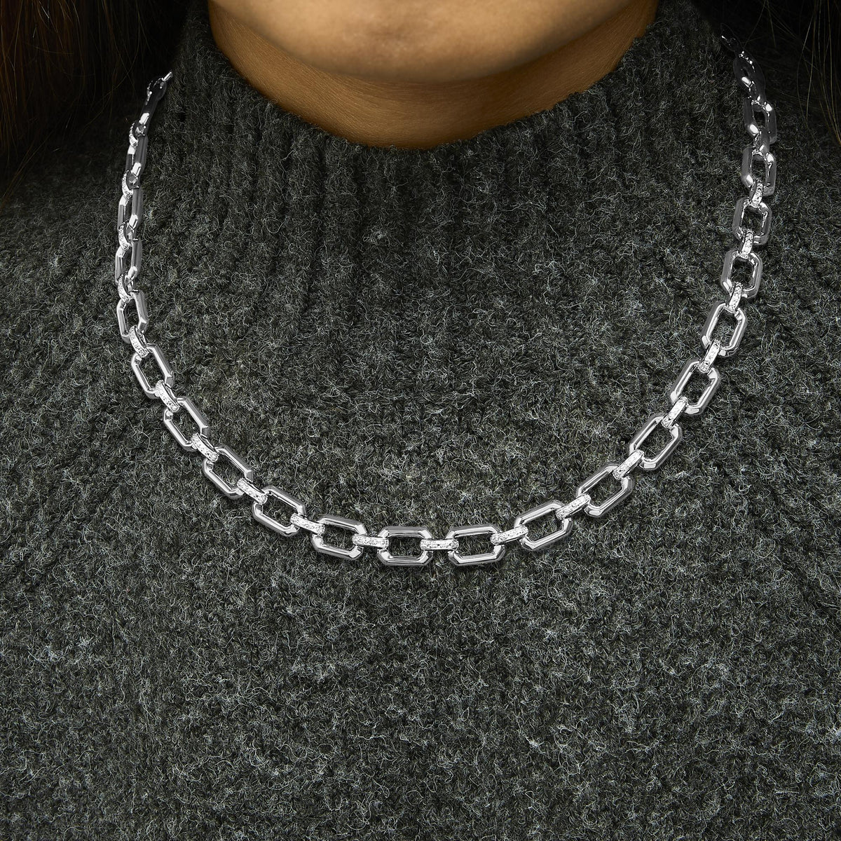 Close-up front view of a white metal necklace with rectangular links, some adorned with pave-set white gemstones, shown worn on a model.