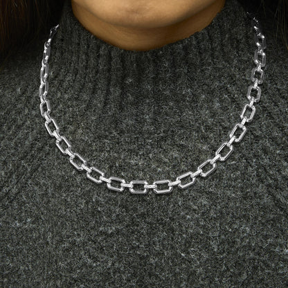 Close-up front view of a white metal necklace with rectangular links, some adorned with pave-set white gemstones, shown worn on a model.