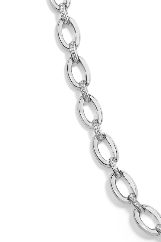 Close-up, angled view of a white metal necklace with oval links connected by smaller links pavé set with round white gemstones.