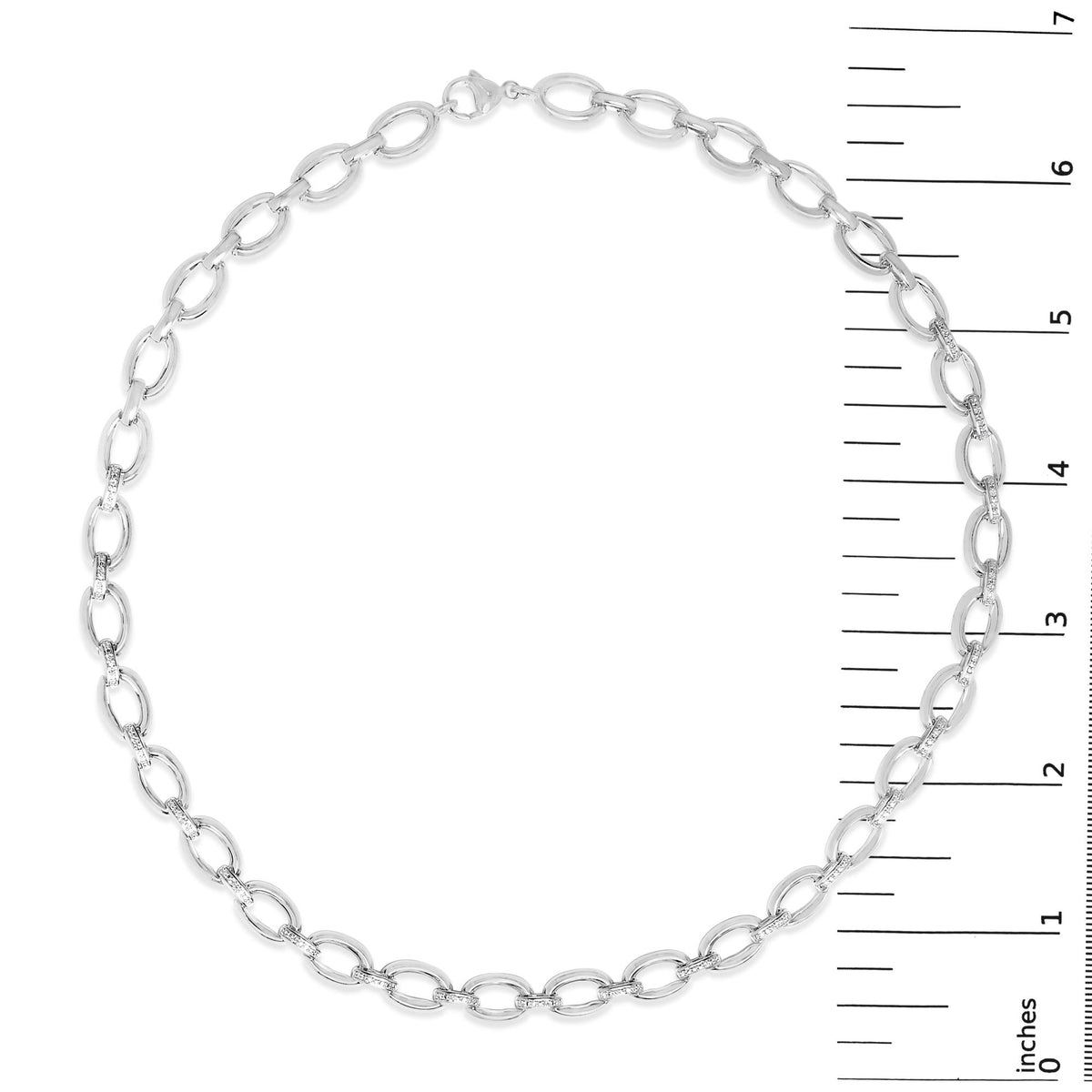 Top-down view of a white metal necklace with oval links, some paved with small white gemstones, shown on a scale.
