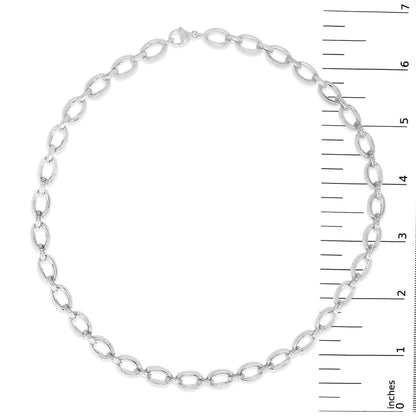 Top-down view of a white metal necklace with oval links, some paved with small white gemstones, shown on a scale.