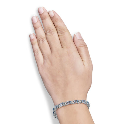 Close-up top view of a wrist wearing a white metal bracelet featuring oval blue gemstones and round white gemstones in prong settings.