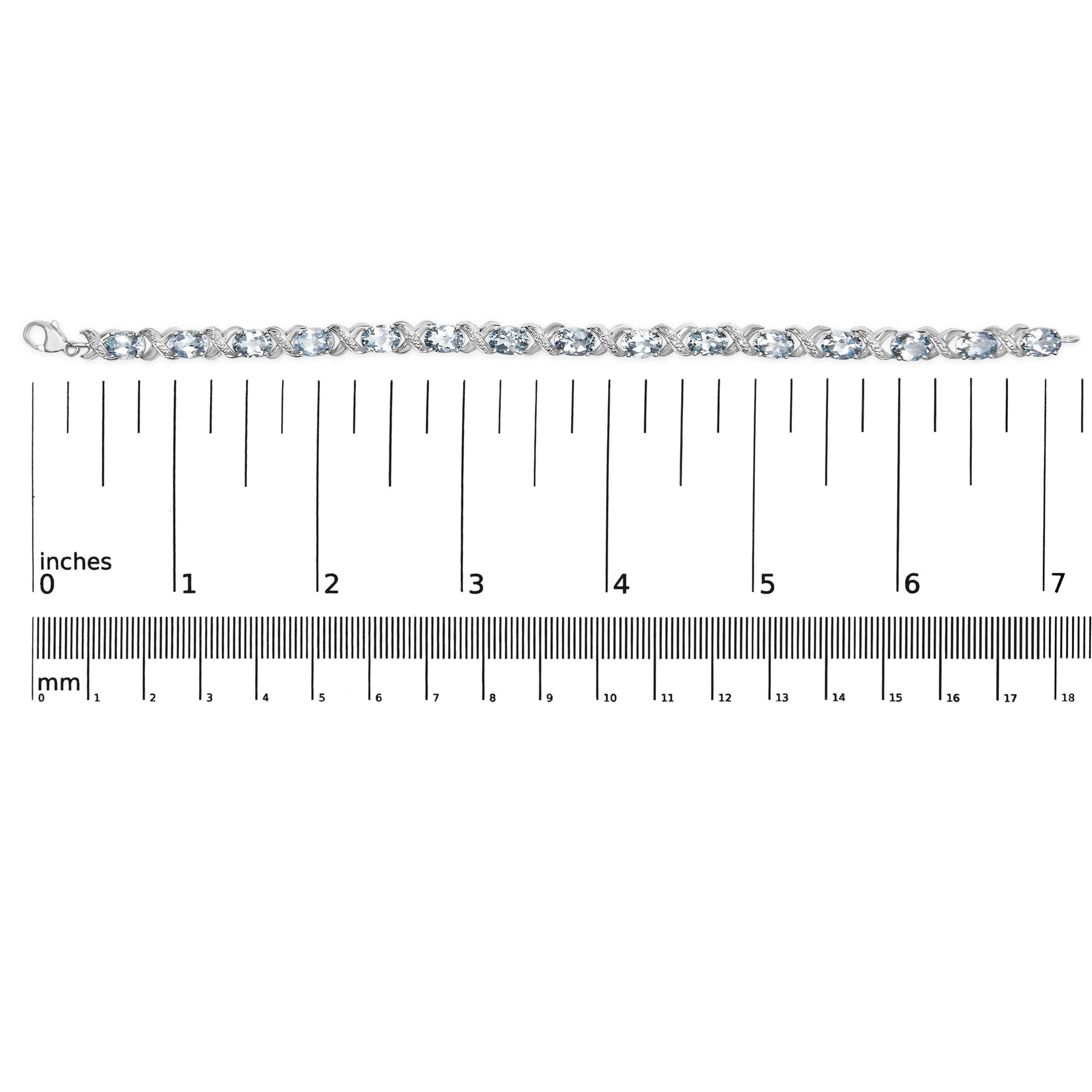 Top-down view of a white metal bracelet with alternating oval blue gemstones and round white gemstones in prong settings, placed on a ruler for size reference.