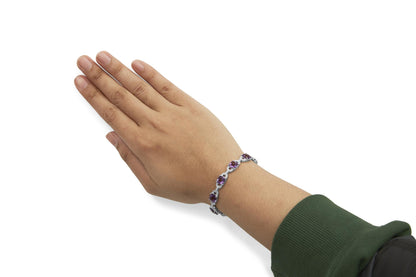 Bracelet with white metal, round white gemstones, and cushion-shaped purple gemstones in prong settings, worn on a model's wrist, angled side view.