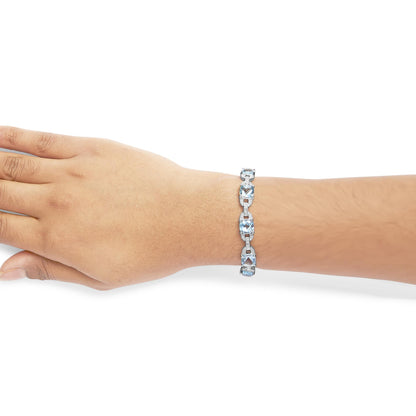 White metal bracelet with cushion-shaped blue gemstones and round white gemstones in prong settings, shown on a model's wrist from a side angle.