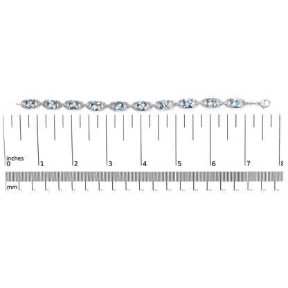 Close-up shot of a white metal bracelet with alternating round white gemstones and cushion-shaped blue gemstones set in prong settings, displayed on a ruler for size reference.