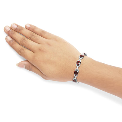White metal bracelet with alternating red cushion-shaped gemstones and round white gemstones in prong settings, shown on a model's wrist from a top angle.
