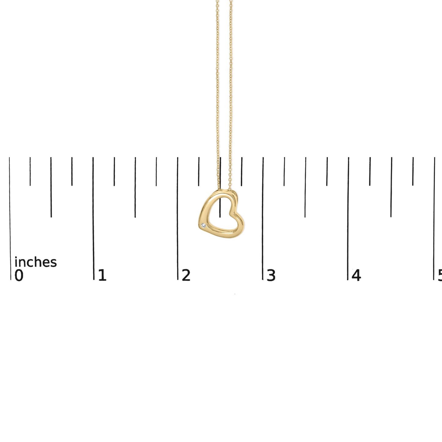 Close-up front view of a yellow metal heart-shaped necklace pendant with a round white gemstone in a bezel setting near the bottom left, shown on a measuring scale.