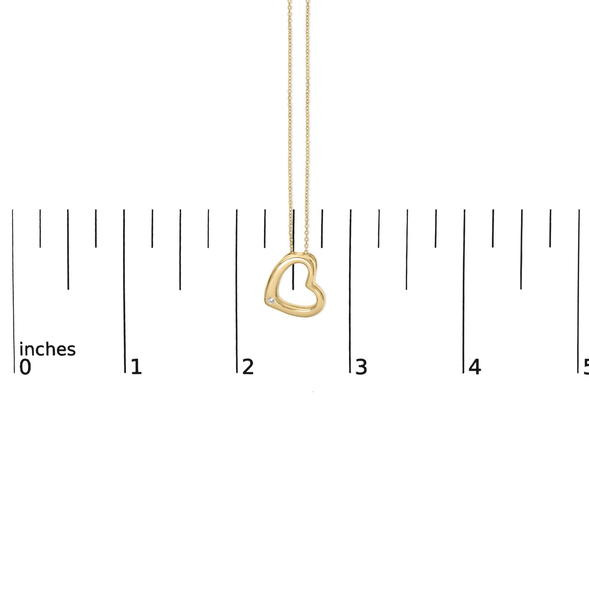 Close-up front view of a yellow metal heart-shaped necklace pendant with a round white gemstone in a bezel setting near the bottom left, shown on a measuring scale.