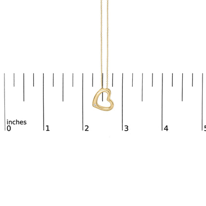 Close-up front view of a yellow metal heart-shaped necklace pendant with a round white gemstone in a bezel setting near the bottom left, shown on a measuring scale.