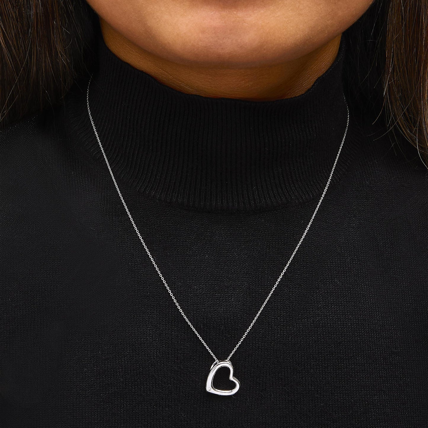Necklace shown worn on a model, featuring a white metal chain and an open heart-shaped pendant with a round white gemstone in bezel setting, shot from the front center at chest level.