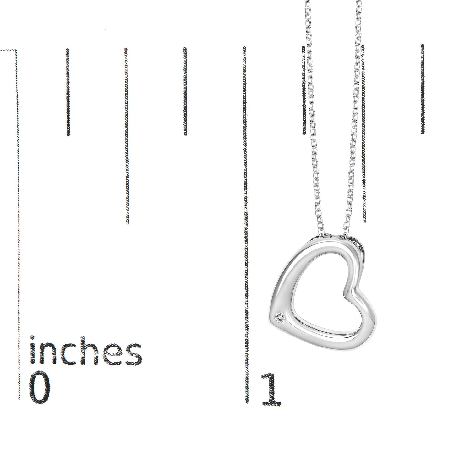 Close-up angled view of a white metal necklace with an open heart-shaped pendant featuring a round white gemstone set in a bezel near the bottom, shown on a scale with measurement markings.