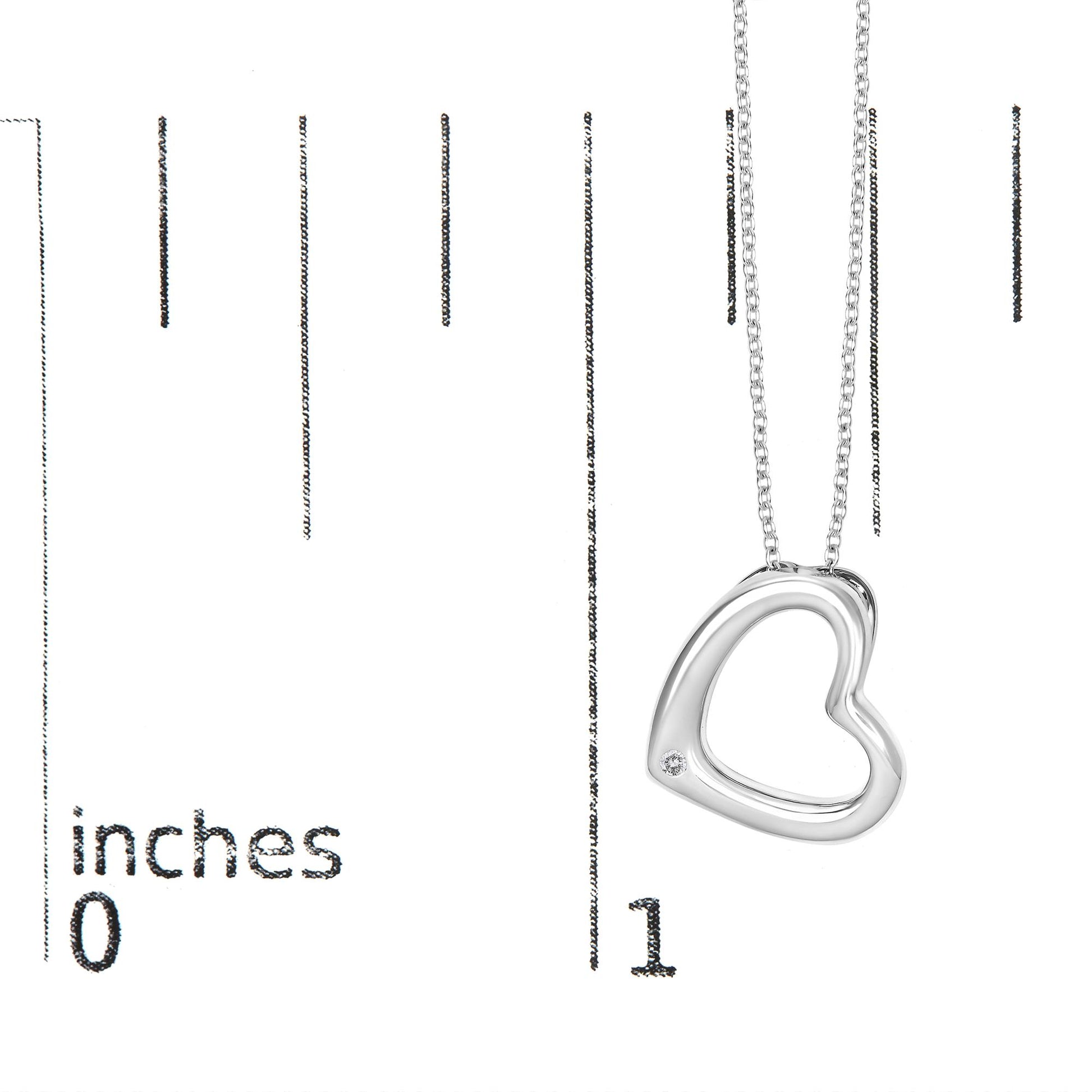Close-up angled view of a white metal necklace with an open heart-shaped pendant featuring a round white gemstone set in a bezel near the bottom, shown on a scale with measurement markings.