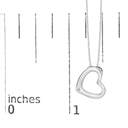Close-up angled view of a white metal necklace with an open heart-shaped pendant featuring a round white gemstone set in a bezel near the bottom, shown on a scale with measurement markings.