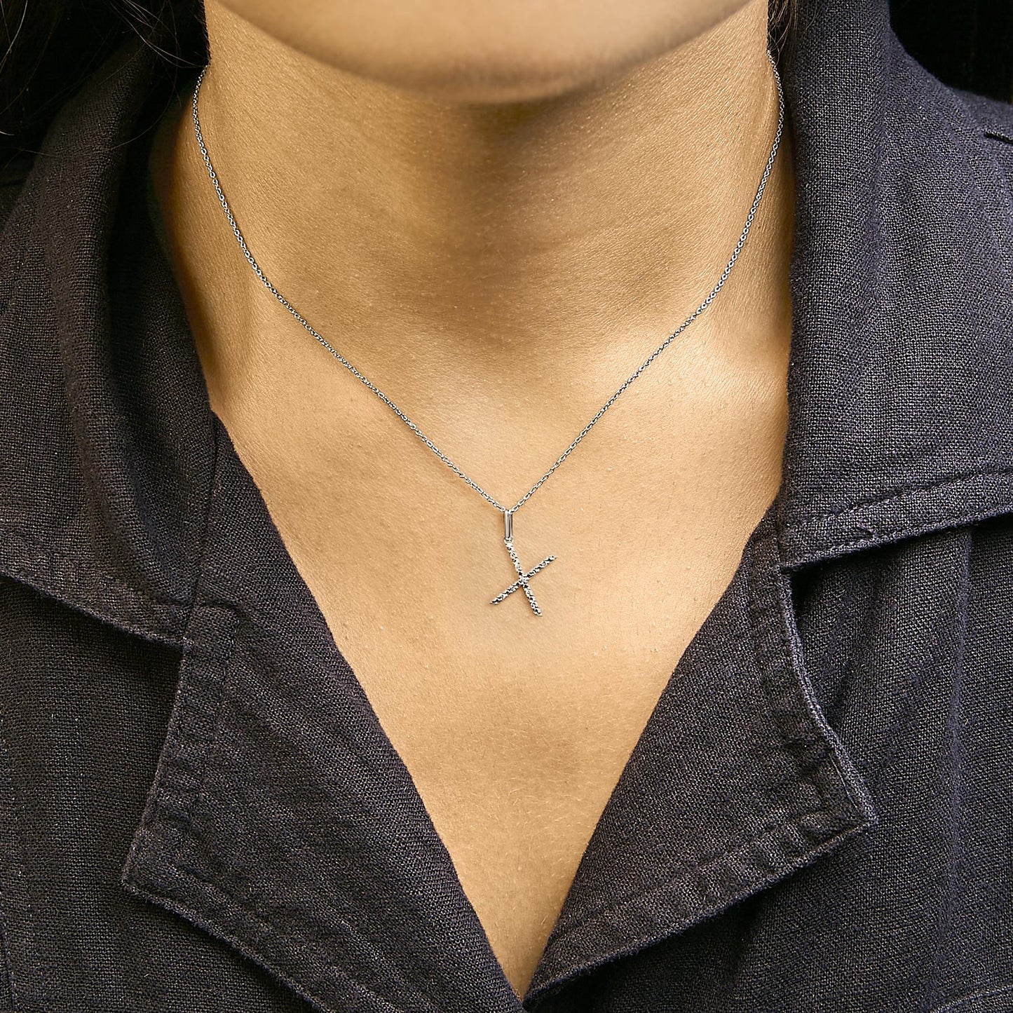 Close-up front view of a model wearing a white metal necklace with a vertical bar pendant adorned with micro-pave white round gemstones.