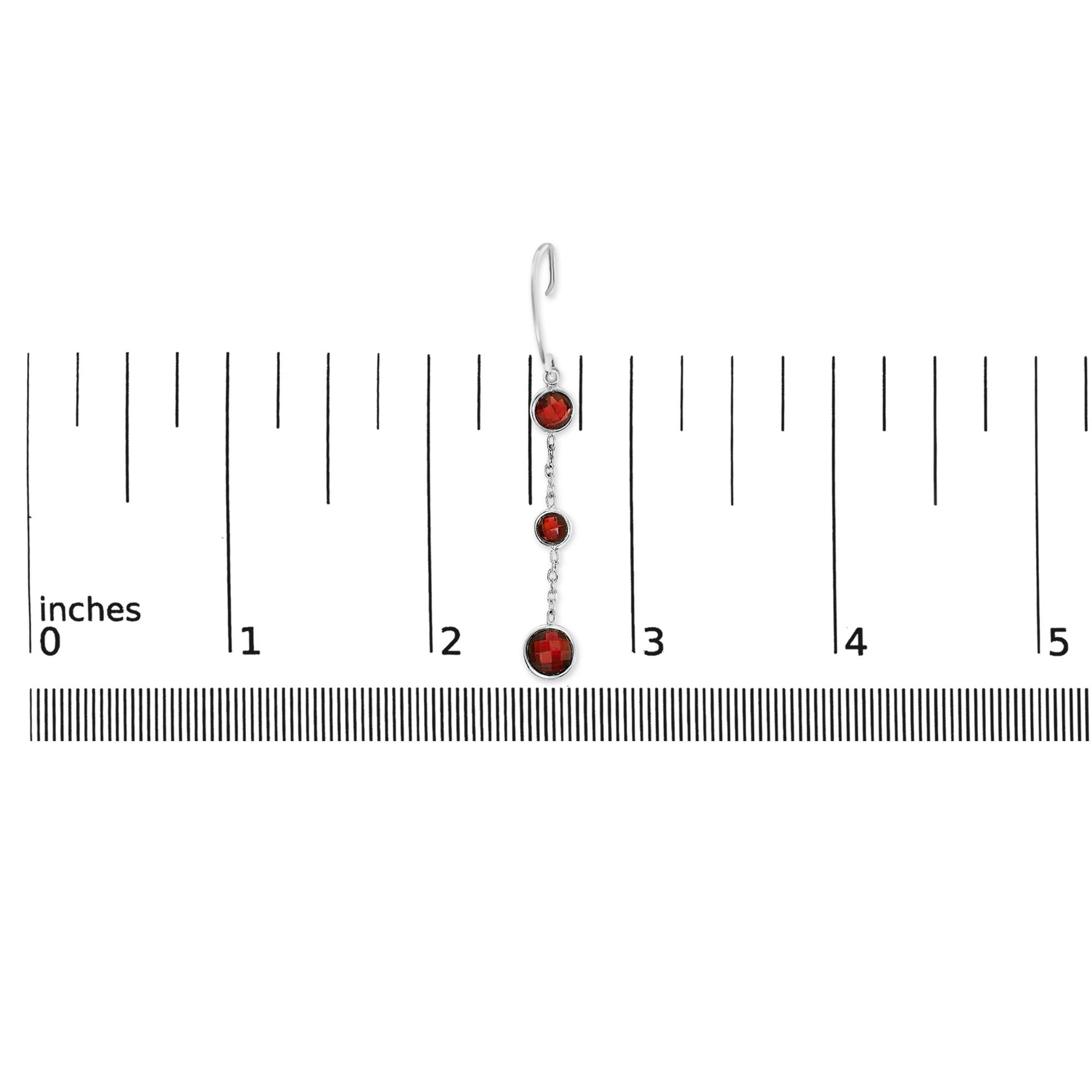 Single white metal earring with three round red gemstones in bezel settings, shown on a ruler for scale, photographed from the front.