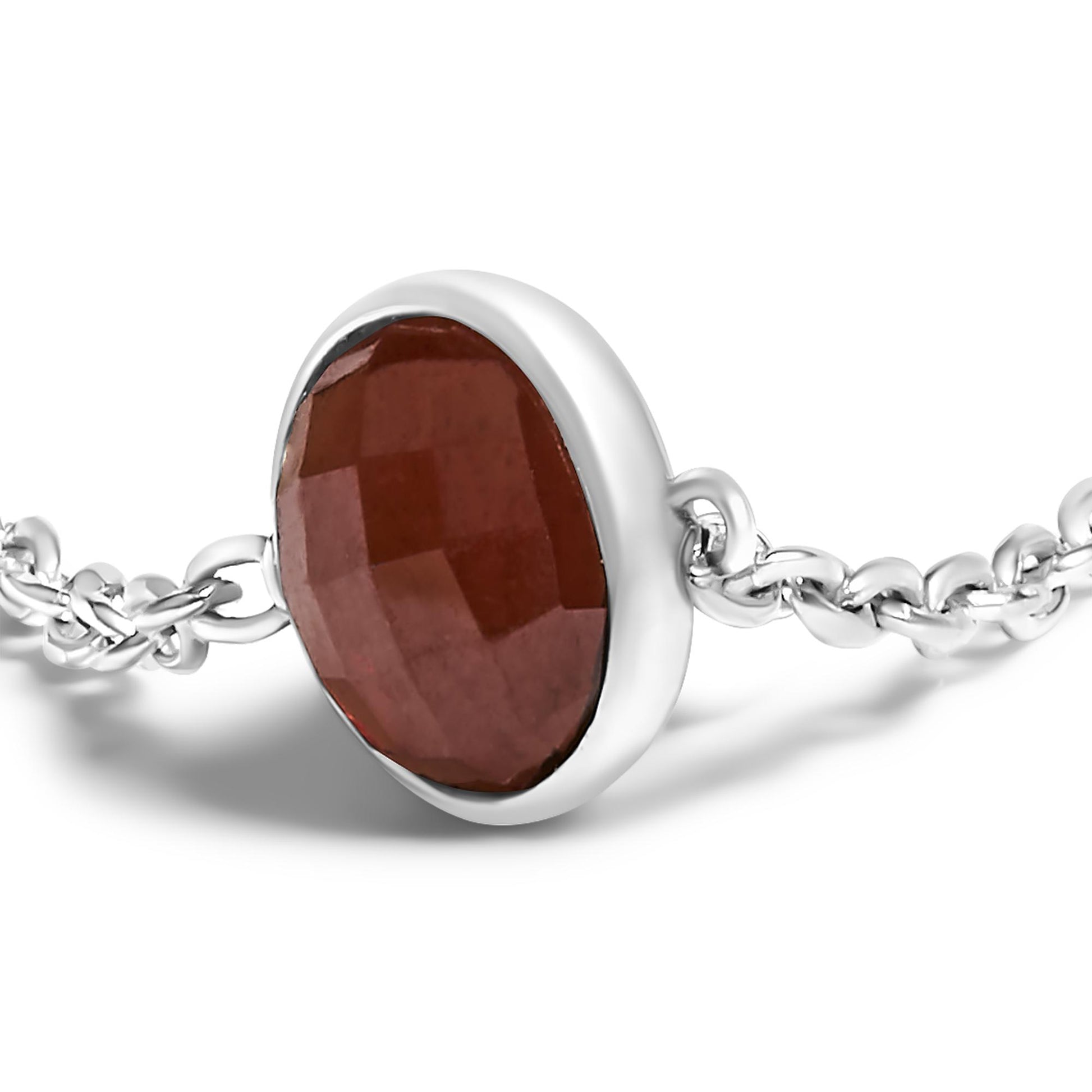 Close-up, angled view of a white metal necklace featuring a round red gemstone in a bezel setting connected to a linked chain.