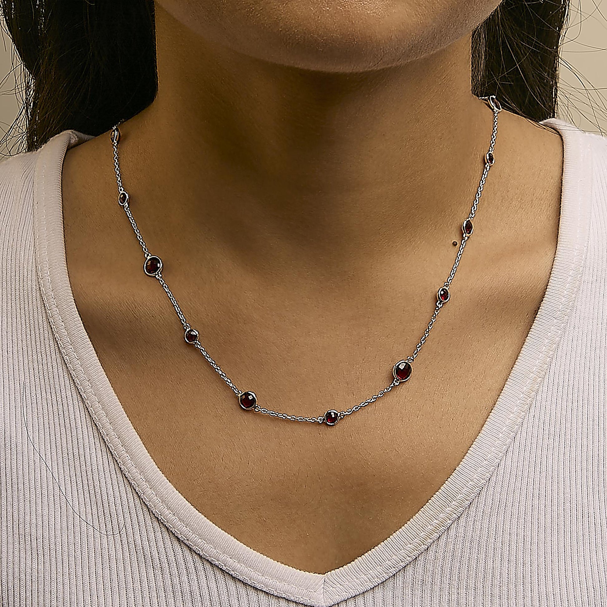 Close-up front view of a white metal necklace with multiple round red gemstones in bezel settings, worn on a model's neck.