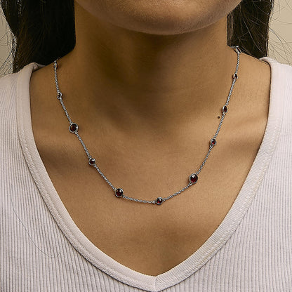 Close-up front view of a white metal necklace with multiple round red gemstones in bezel settings, worn on a model's neck.