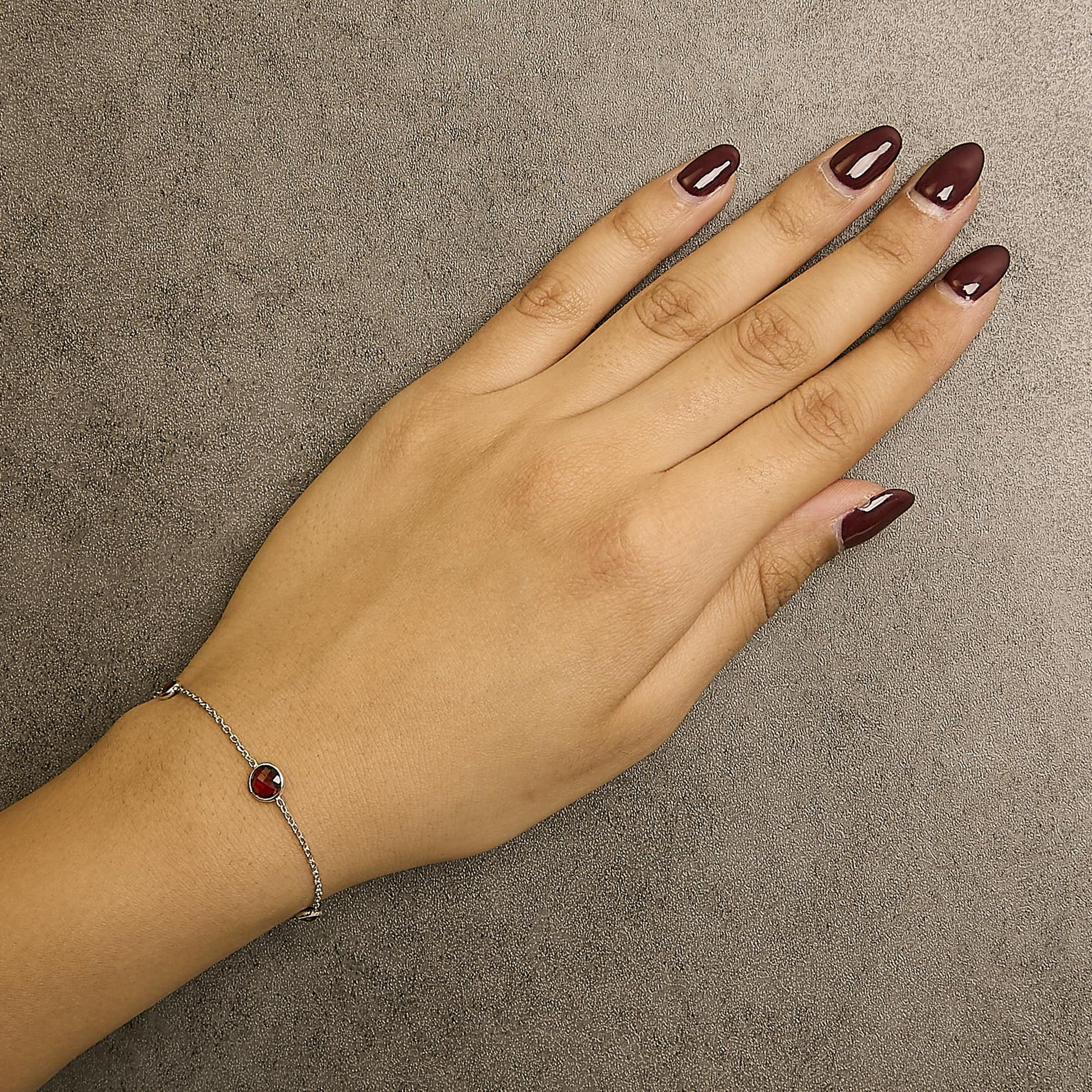 Close-up angled top view of a white metal bracelet with round red gemstones in bezel settings, worn on a model's wrist.