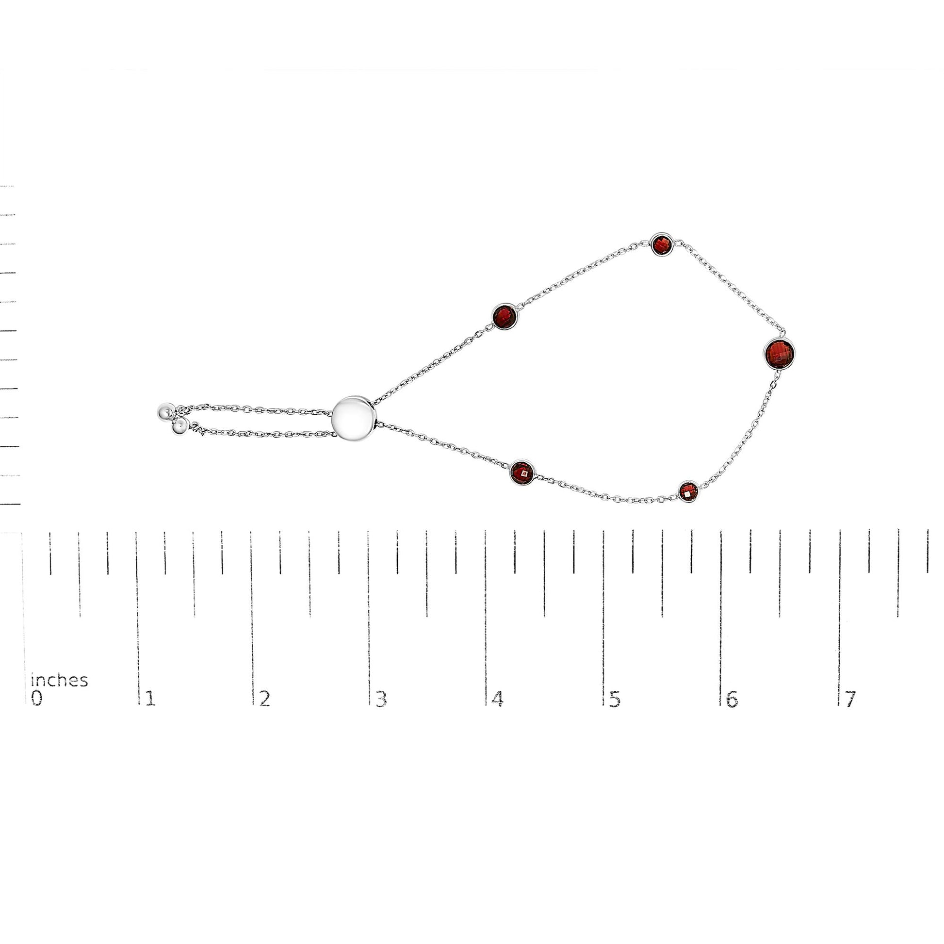 White metal bracelet with round red gemstones in bezel settings, displayed flat on a ruler for size reference, top-down angle.