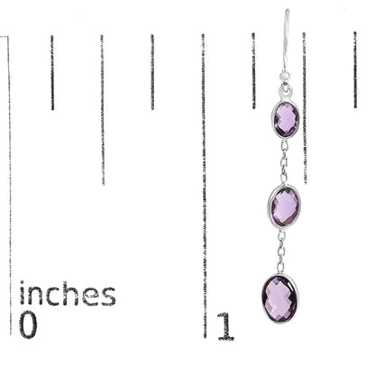 Close-up front view of a white metal dangle earring with three oval purple gemstones in bezel settings, shown against a ruler for size reference.