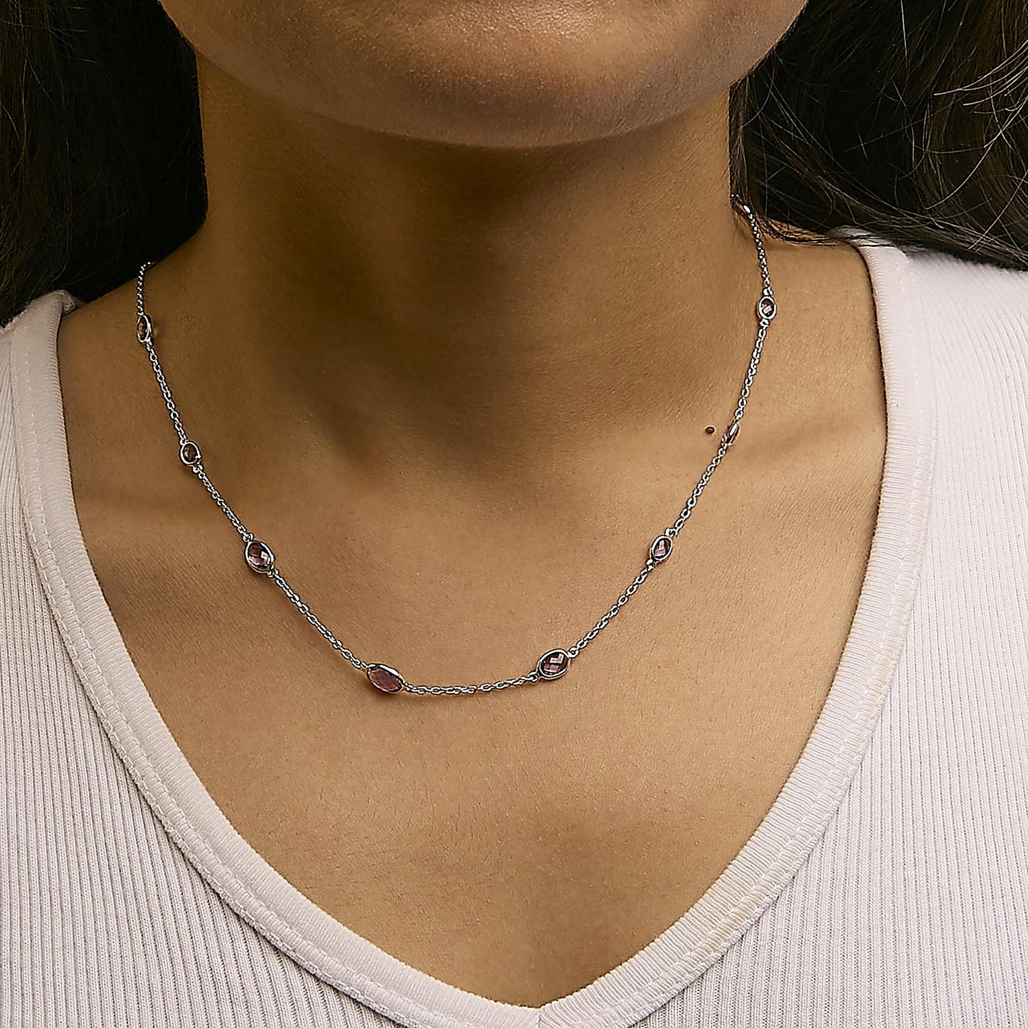 Close-up front view of a white metal necklace with multiple oval purple gemstones in bezel settings, worn on a model.