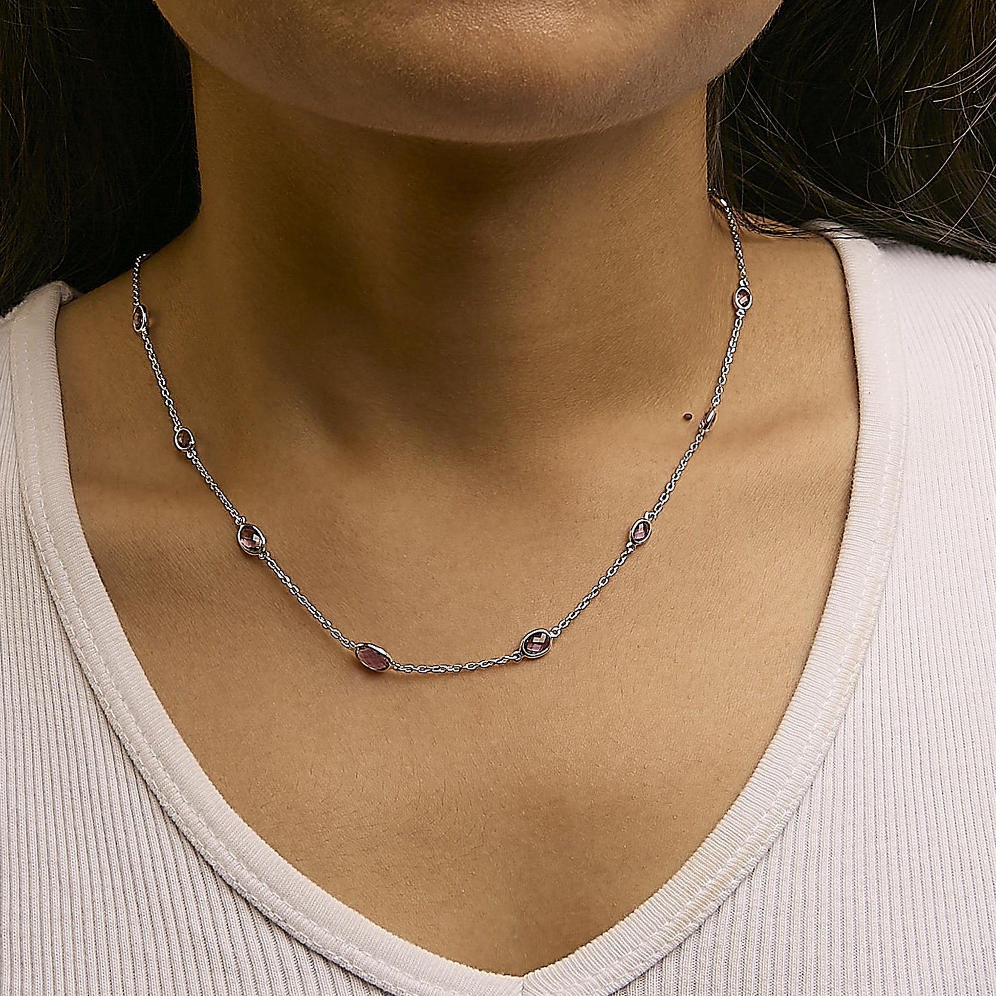 Close-up front view of a white metal necklace with multiple oval purple gemstones in bezel settings, worn on a model.