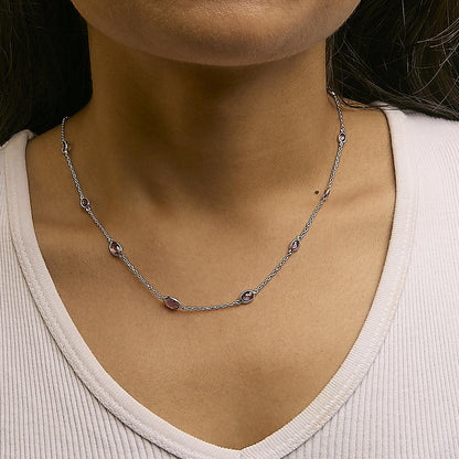 Close-up front view of a white metal necklace with multiple oval purple gemstones in bezel settings, worn on a model.