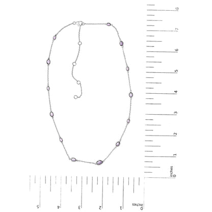 White necklace with oval purple gemstones in bezel settings evenly spaced along a fine chain, displayed flat on a white background alongside a ruler for size reference, shot from above.
