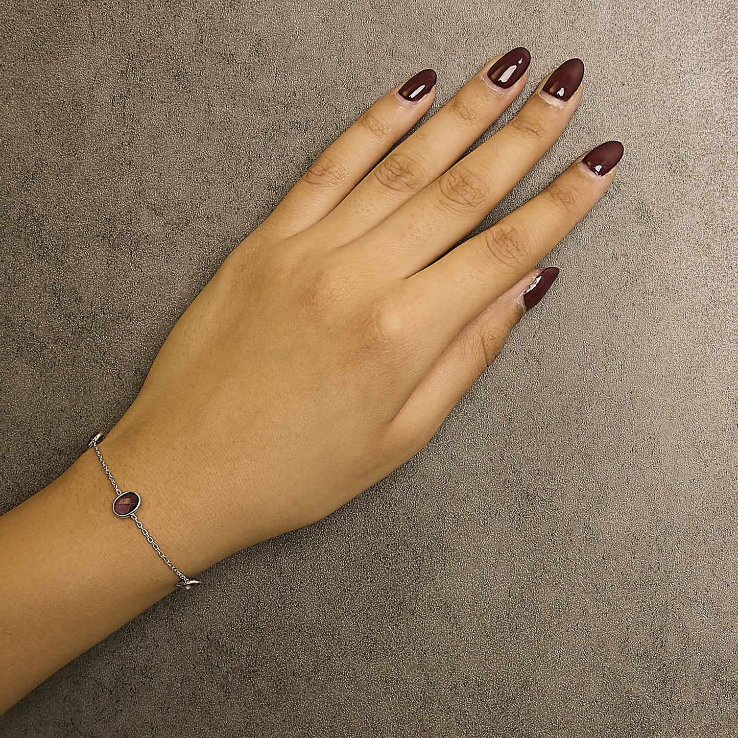 Close-up top view of a white metal bracelet with oval purple gemstones in bezel settings, worn on a model's wrist.