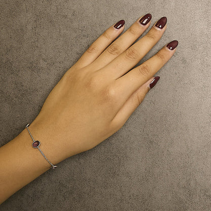 Close-up top view of a white metal bracelet with oval purple gemstones in bezel settings, worn on a model's wrist.