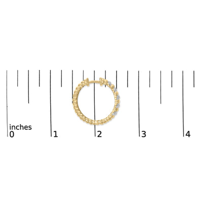Close-up front angle of a yellow metal round hoop earring with white gemstones in a pave setting shown on a ruler scale.