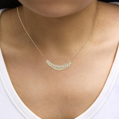 Close-up front view of a yellow metal necklace with a curved bar pendant featuring alternating sections of pave-set white gemstones, worn on a model's neck.