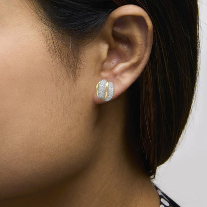 Close-up side view of a model wearing rounded earrings featuring alternating bands of yellow metal and white gemstones in a prong setting.