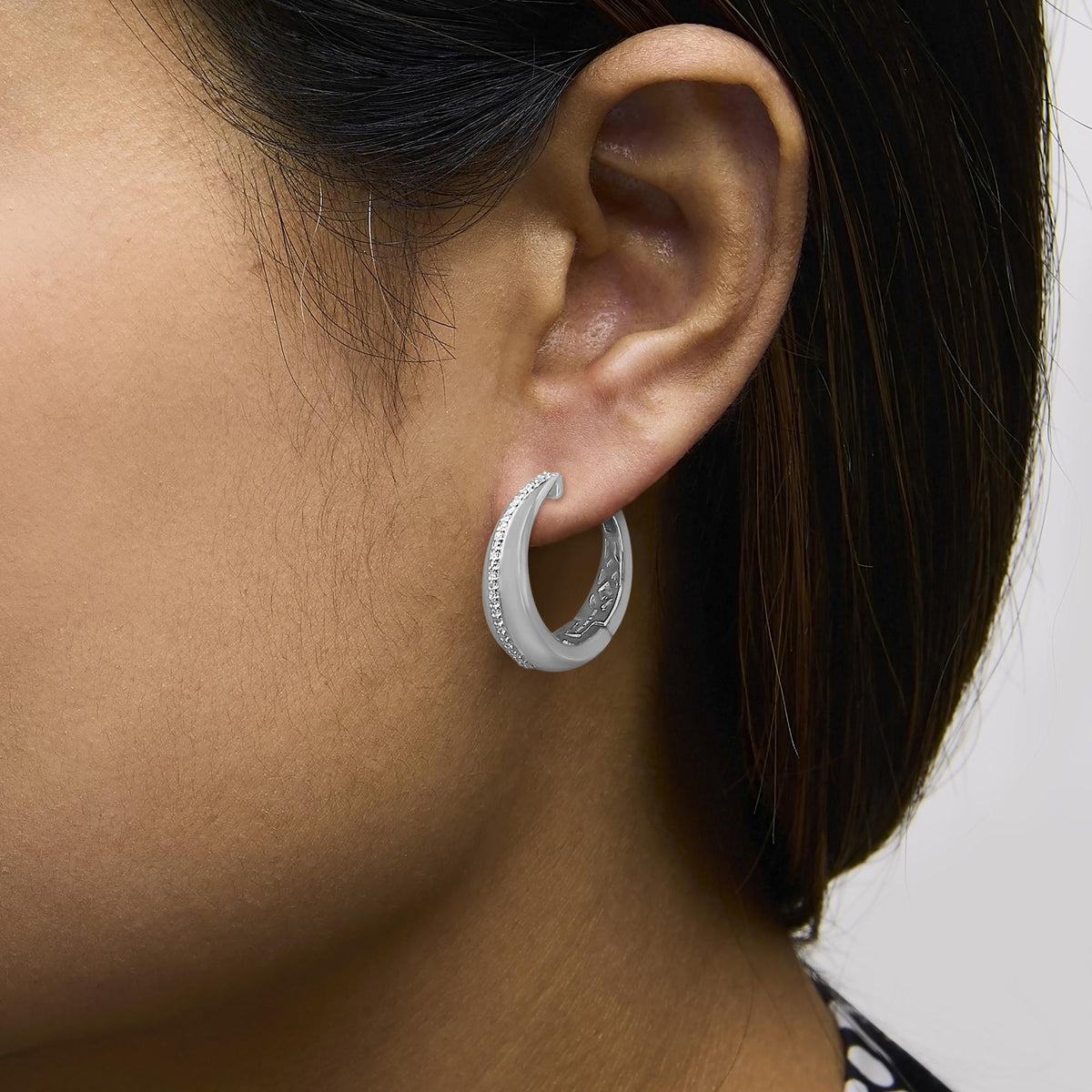 Close-up side view of a model wearing white metal hoop earrings adorned with round white gemstones in a prong setting along the outer edge.