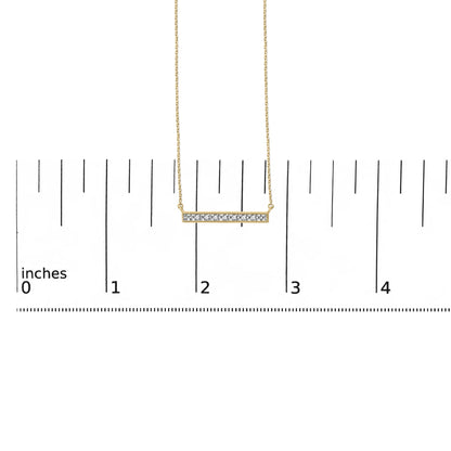 Close-up front view of a yellow metal necklace with a horizontal bar pendant set with seven round white gemstones in prong settings, shown on a ruler scale background.
