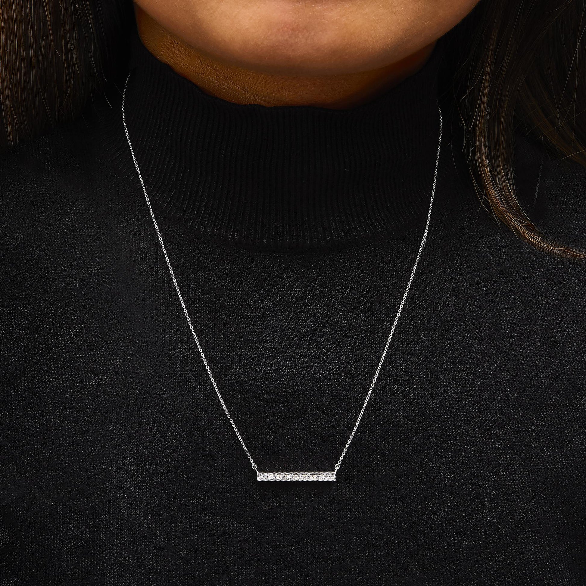 White metal necklace with a horizontal bar pendant set with round white gemstones in prong settings, shown worn on a model from a front angle.