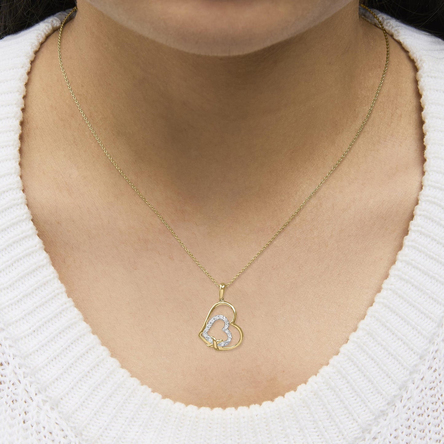 Yellow metal necklace with two heart-shaped pendants, one outlined with white gemstones in pave setting, shown worn on a model, close-up front angle.