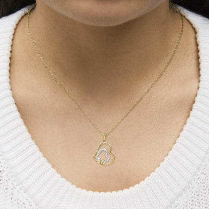 Yellow metal necklace with two heart-shaped pendants, one outlined with white gemstones in pave setting, shown worn on a model, close-up front angle.