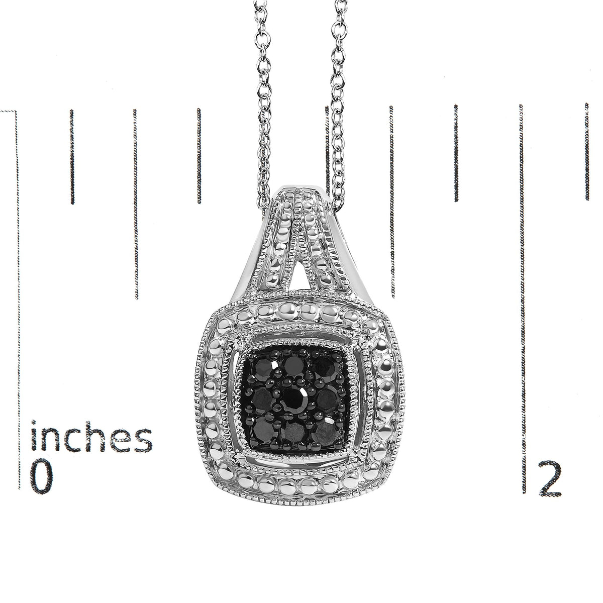 Close-up front view of a white metal necklace pendant with a cluster of black gemstones in the center and additional decorative elements surrounding it, shown on a scale background.