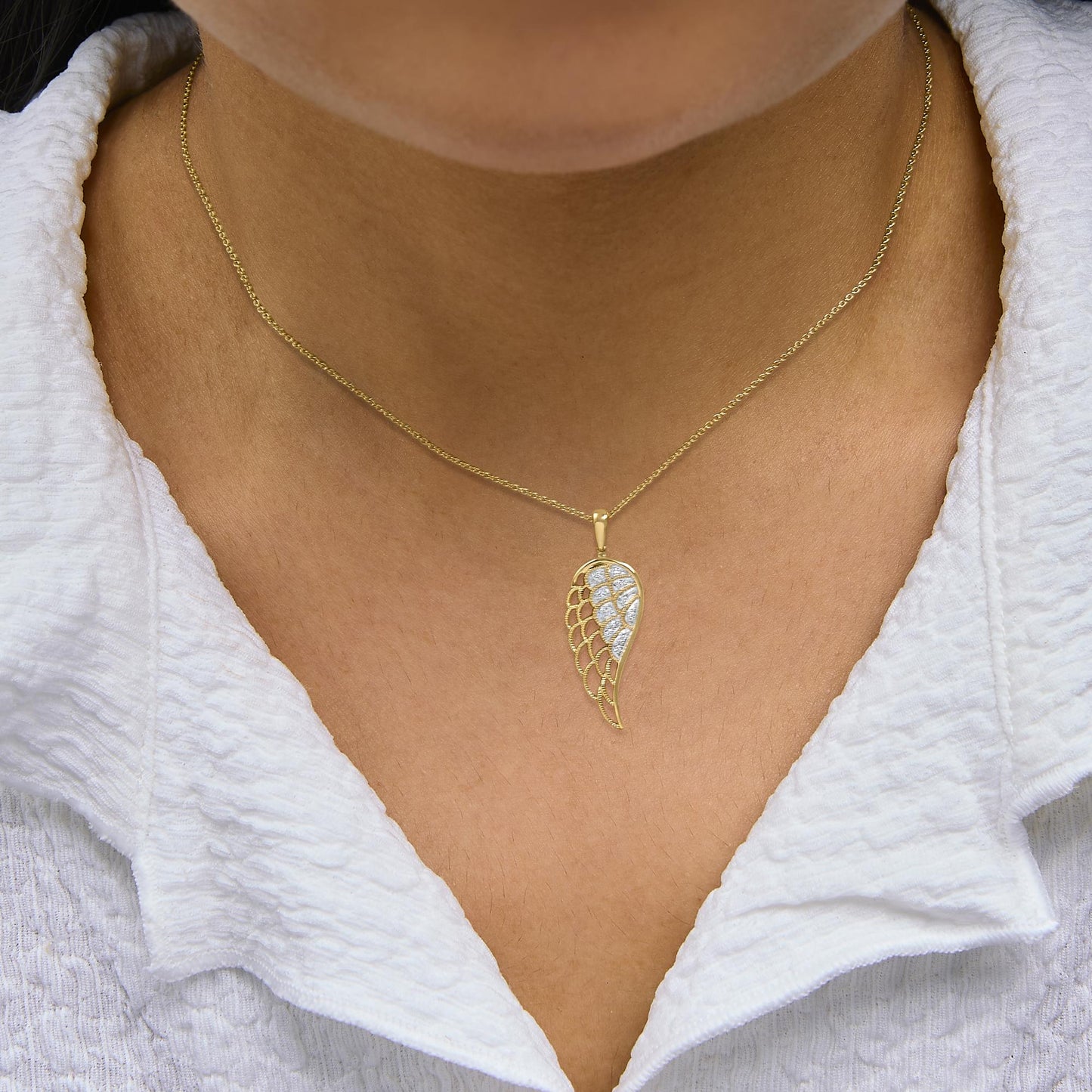 Close-up front view of a yellow metal necklace with a wing-shaped pendant featuring pave-set white gemstones, shown worn on a model.