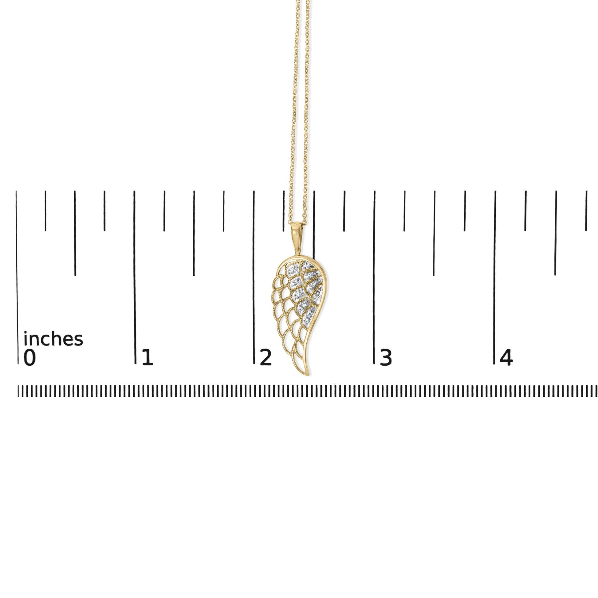 Close-up front angle of a yellow metal necklace pendant with a wing-shaped design featuring multiple white gemstones in a pave setting, shown on a measurement scale.