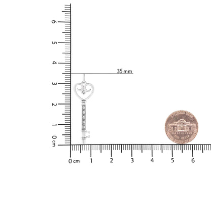 White metal necklace pendant in key shape with heart-shaped bow and round brownish gemstones in pave and bezel settings, shown upright on a ruler and scale for size reference.