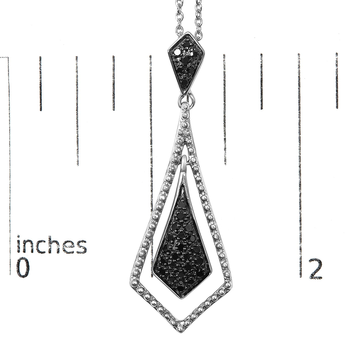 Close-up front view of a white metal necklace pendant featuring geometric shapes decorated with round black gemstones in pave setting, shown on a measurement scale.
