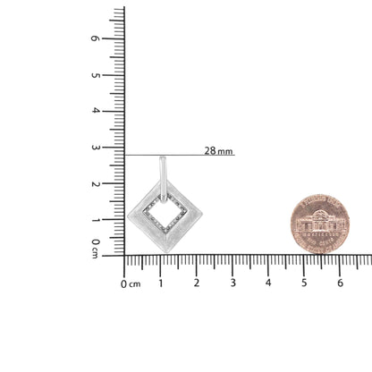 Front angled shot of a white metal necklace pendant with a square-shaped design, featuring an inner square adorned with round white gemstones in a pave setting, placed on a ruler and next to a coin for size reference.