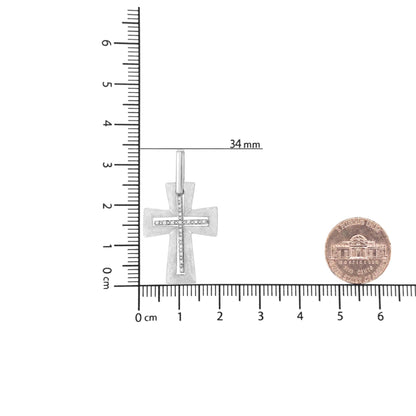 White metal cross-shaped necklace pendant with white round prong-set gemstones in a vertical and horizontal line, shown from the front on a ruler for size reference.