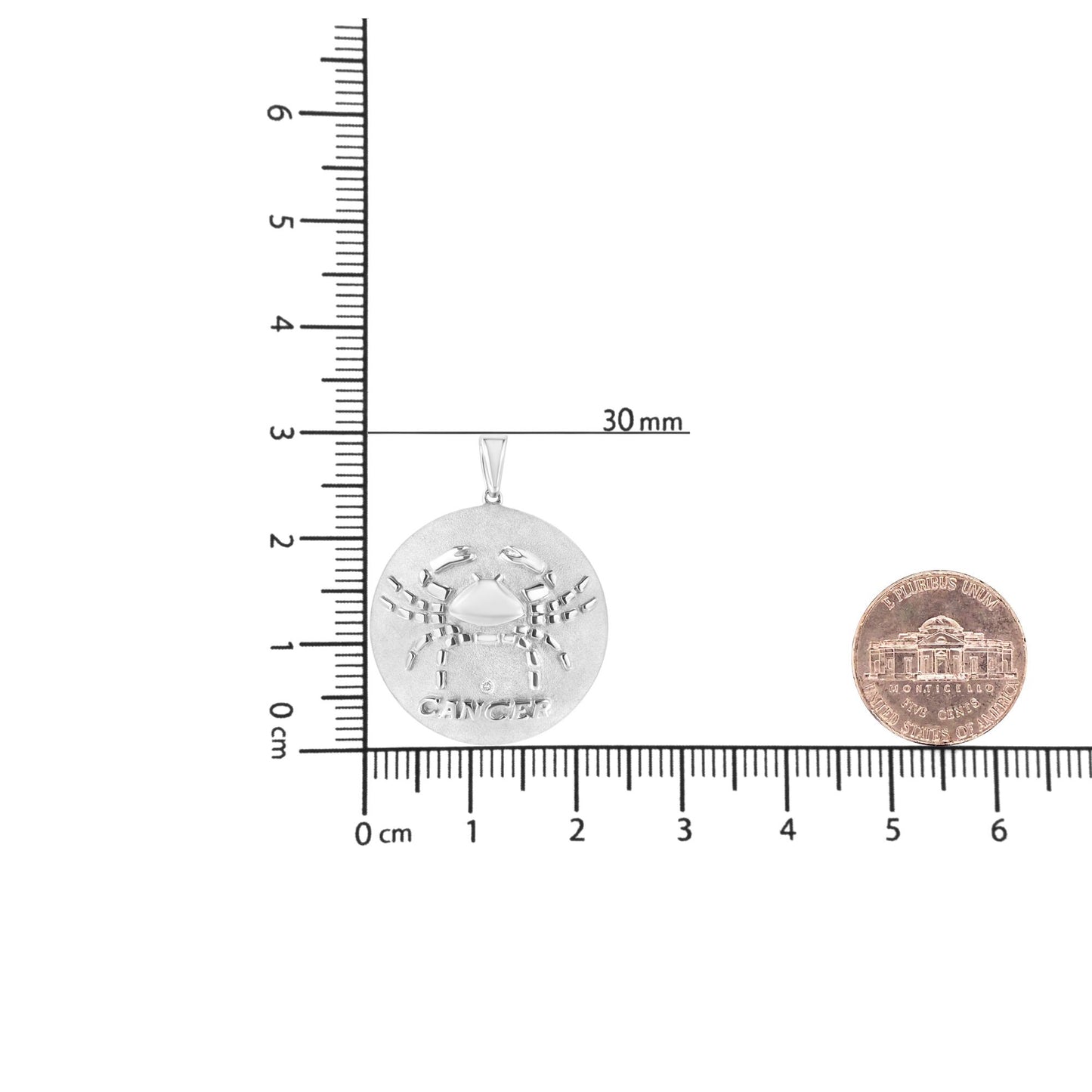 Round white metal pendant necklace with raised crab design and 'CANCER' text, featuring one small round brownish gemstone in bezel setting, shown flat on a ruler for size reference.